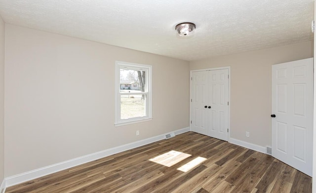 unfurnished bedroom featuring a textured ceiling, a closet, baseboards, and dark wood-style flooring