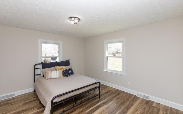 bedroom featuring visible vents, a textured ceiling, baseboards, and wood finished floors