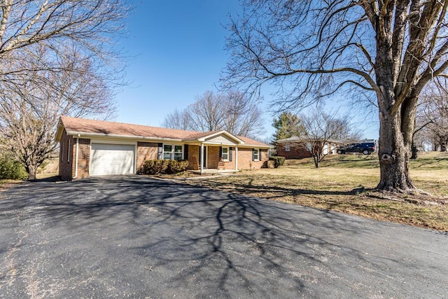 single story home featuring aphalt driveway, a front yard, brick siding, and a garage