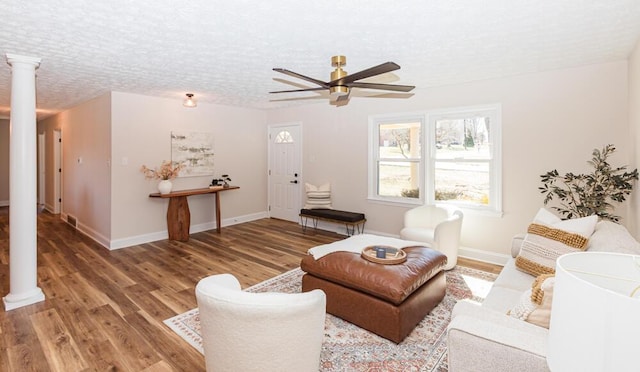 living area featuring a textured ceiling, baseboards, wood finished floors, and ornate columns