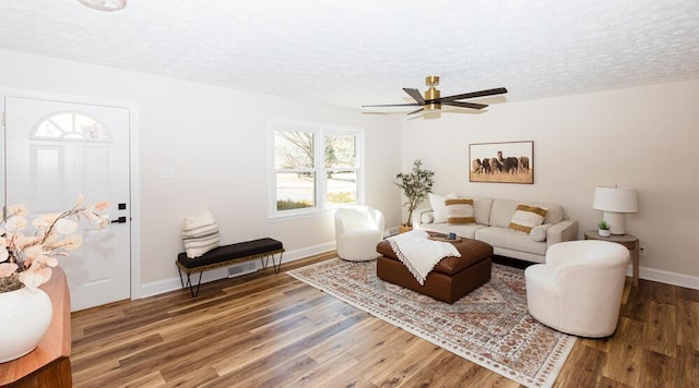 living area featuring a textured ceiling, ceiling fan, wood finished floors, and baseboards