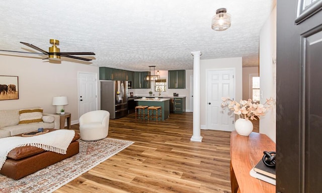 living area featuring a textured ceiling, ceiling fan, light wood-style flooring, baseboards, and ornate columns