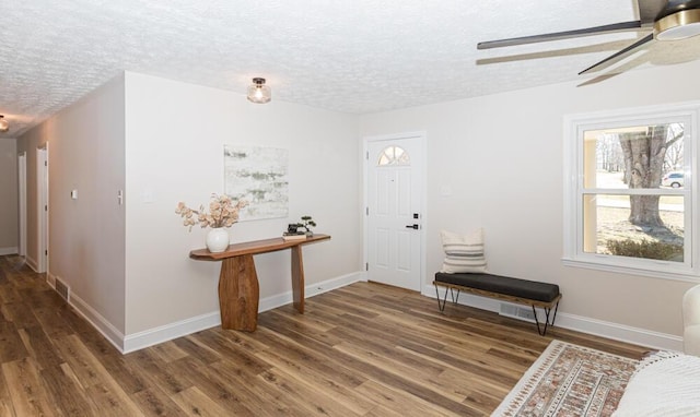 foyer entrance featuring a textured ceiling, wood finished floors, visible vents, and baseboards