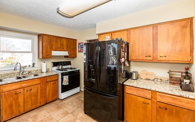 kitchen featuring gas range gas stove, sink, black refrigerator with ice dispenser, light stone counters, and a textured ceiling