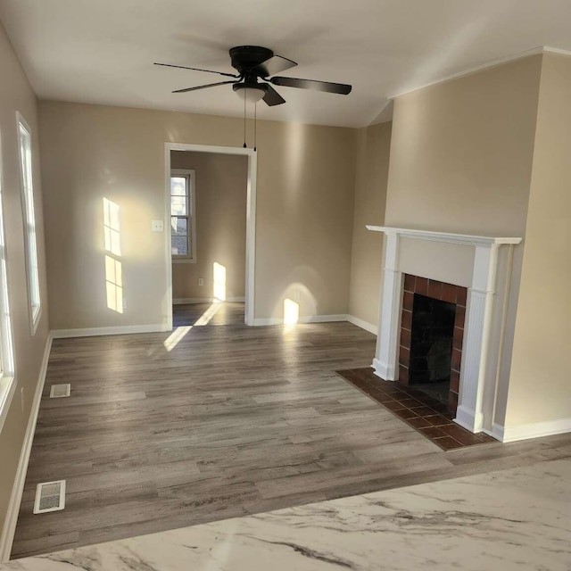 unfurnished living room with ceiling fan, a healthy amount of sunlight, dark wood-type flooring, and a tile fireplace