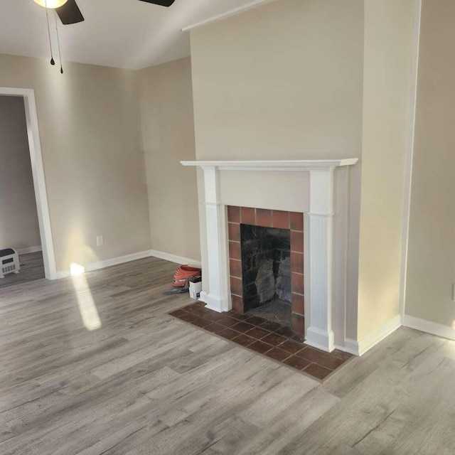 unfurnished living room featuring ceiling fan, wood-type flooring, and a tiled fireplace