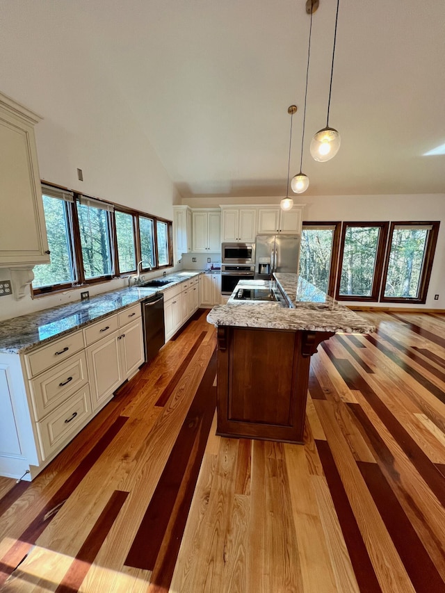 kitchen with light stone countertops, stainless steel appliances, a center island with sink, and decorative light fixtures