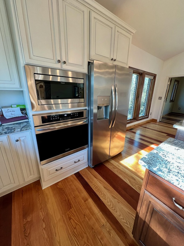 kitchen with white cabinetry, light hardwood / wood-style floors, appliances with stainless steel finishes, lofted ceiling, and stone countertops