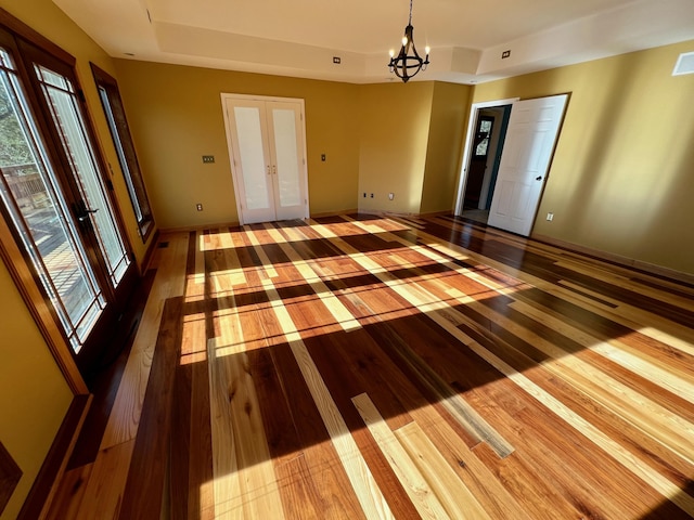 unfurnished room featuring hardwood / wood-style floors, french doors, and an inviting chandelier