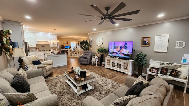 living room featuring dark wood-type flooring, crown molding, and ceiling fan with notable chandelier