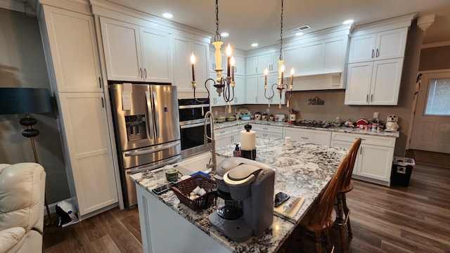 kitchen featuring light stone countertops, pendant lighting, stainless steel appliances, a center island with sink, and white cabinetry