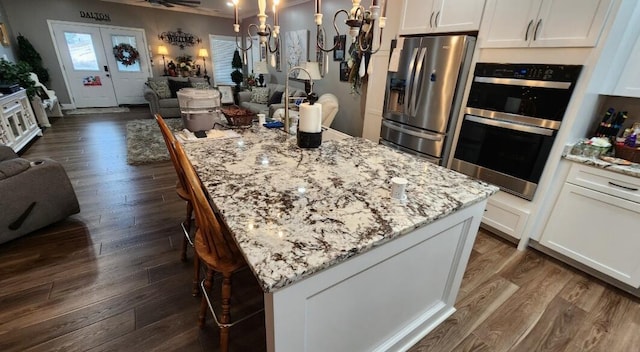 kitchen featuring stainless steel appliances, white cabinetry, light stone counters, a center island with sink, and pendant lighting