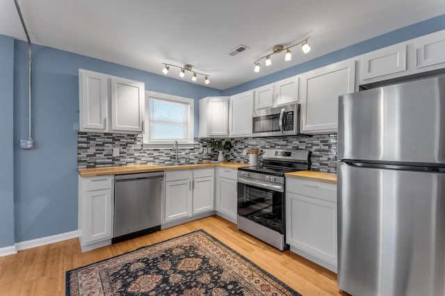 kitchen with butcher block countertops, white cabinets, and appliances with stainless steel finishes