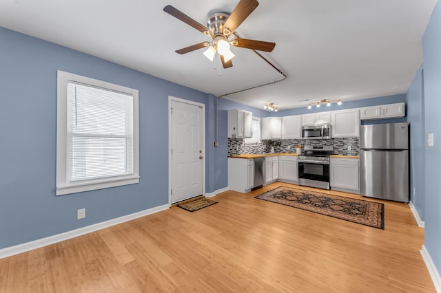 kitchen with ceiling fan, light wood-type flooring, appliances with stainless steel finishes, tasteful backsplash, and white cabinetry