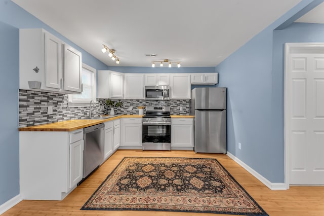 kitchen with wood counters, tasteful backsplash, stainless steel appliances, sink, and white cabinetry