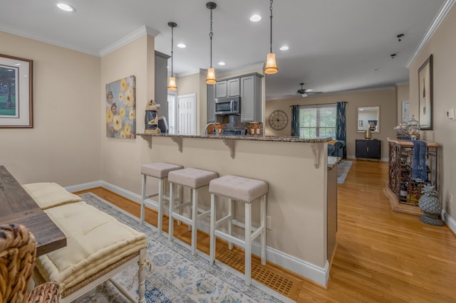 kitchen featuring gray cabinetry, decorative light fixtures, light hardwood / wood-style floors, kitchen peninsula, and a breakfast bar area