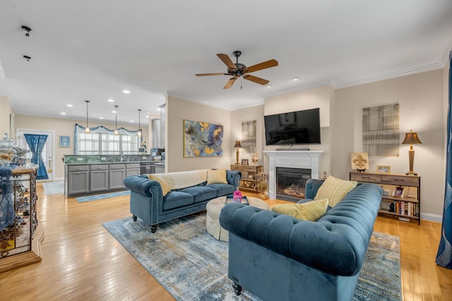 living room featuring light hardwood / wood-style floors, ceiling fan, crown molding, and sink