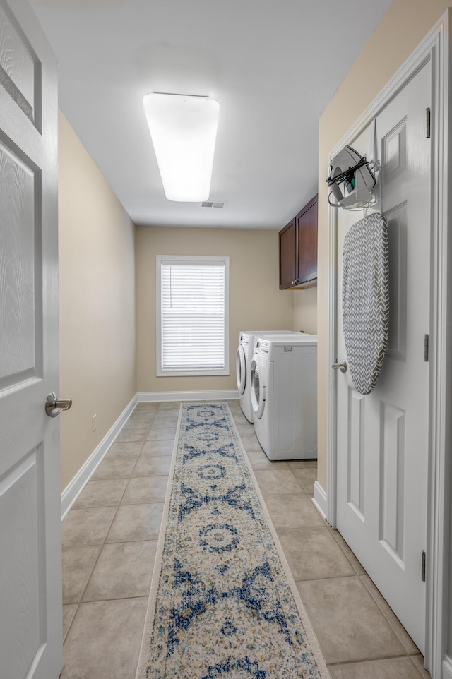 laundry area featuring washing machine and dryer, light tile patterned floors, and cabinets