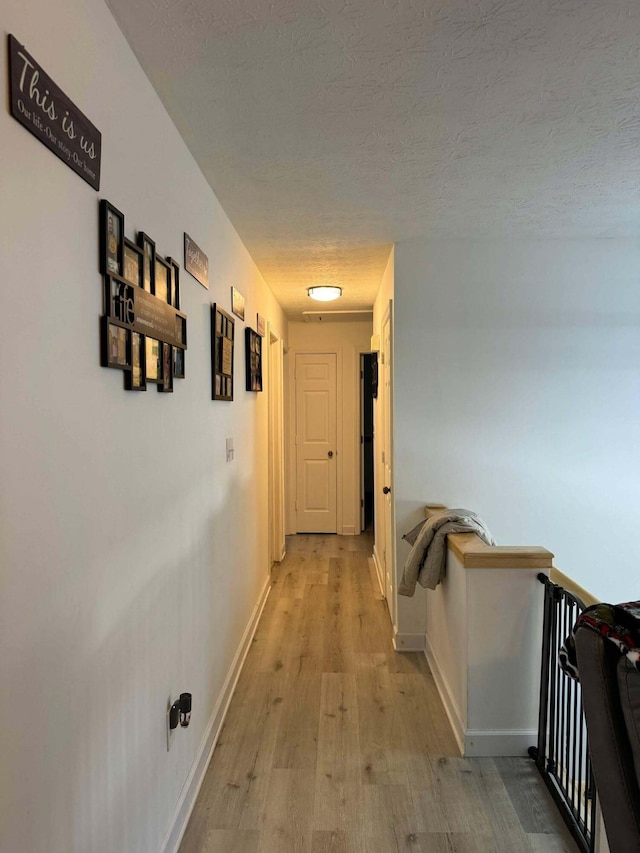 hallway with light wood-type flooring and a textured ceiling