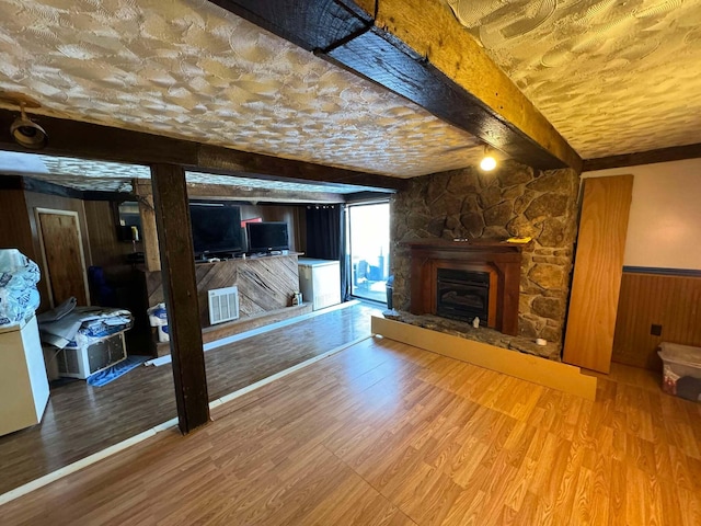 living room featuring beamed ceiling, wood-type flooring, a stone fireplace, and wood walls