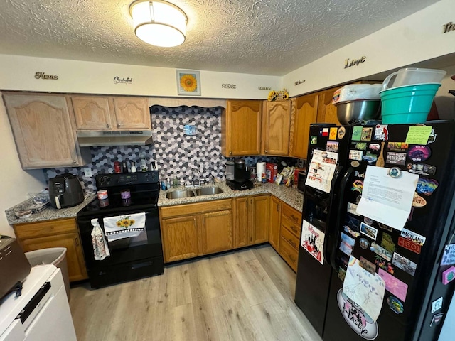 kitchen featuring backsplash, black appliances, sink, light wood-type flooring, and a textured ceiling