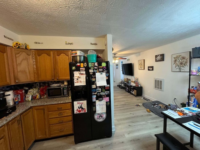 kitchen featuring black refrigerator with ice dispenser, ceiling fan, light hardwood / wood-style floors, and a textured ceiling