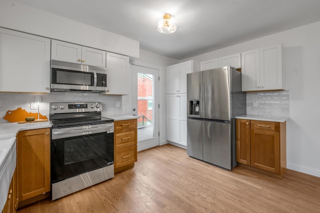 kitchen with tasteful backsplash, white cabinetry, light hardwood / wood-style flooring, and appliances with stainless steel finishes