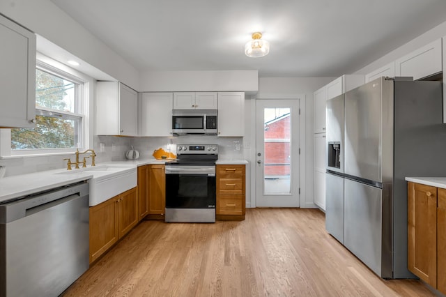 kitchen with white cabinetry, sink, light hardwood / wood-style flooring, backsplash, and appliances with stainless steel finishes