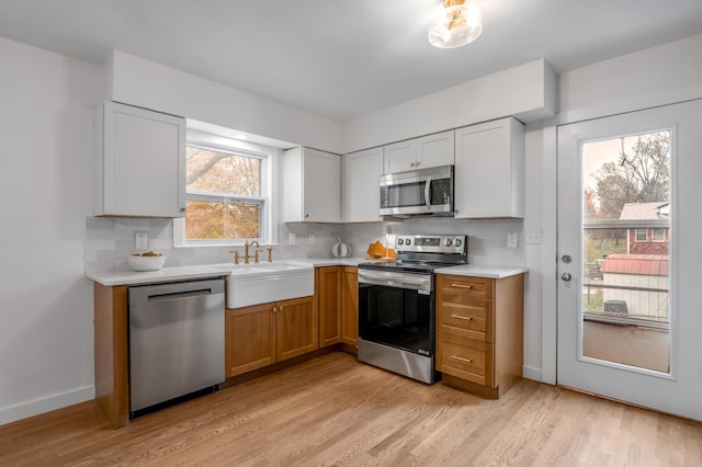 kitchen featuring white cabinetry, sink, decorative backsplash, appliances with stainless steel finishes, and light wood-type flooring