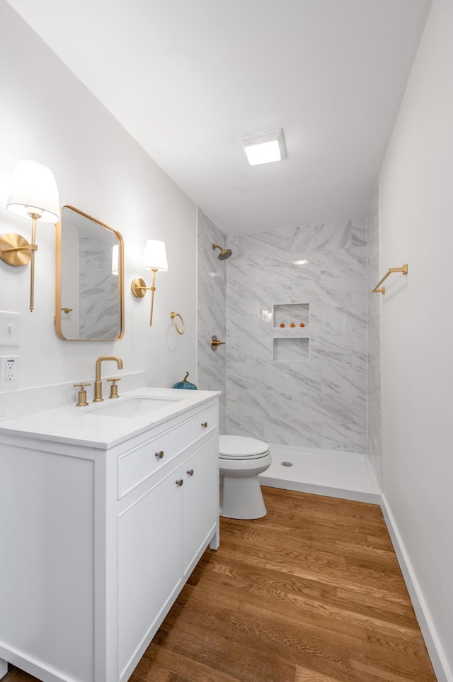 bathroom featuring a tile shower, hardwood / wood-style floors, vanity, and toilet