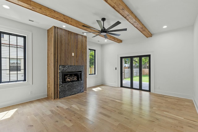 unfurnished living room featuring a premium fireplace, beamed ceiling, light hardwood / wood-style floors, and ceiling fan