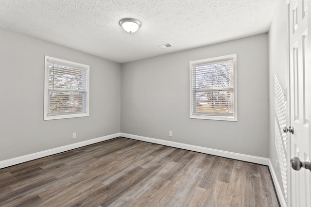 empty room with a textured ceiling, plenty of natural light, and hardwood / wood-style flooring