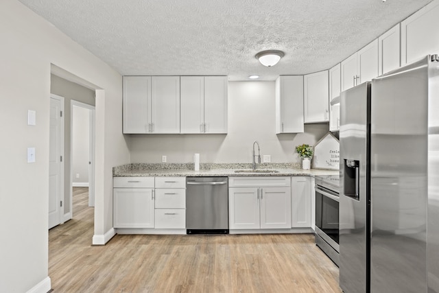 kitchen with stainless steel appliances, light stone counters, sink, light hardwood / wood-style flooring, and white cabinetry