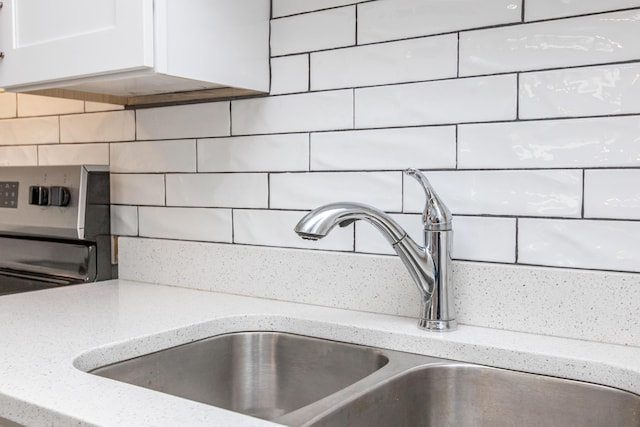 interior details with white cabinets, light stone countertops, sink, and tasteful backsplash