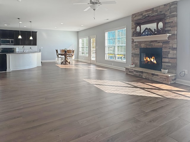 unfurnished living room with a fireplace, dark wood-type flooring, sink, and ceiling fan