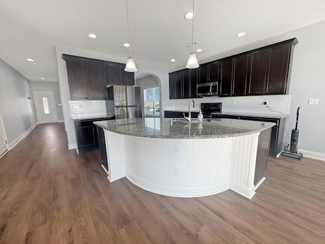 kitchen featuring wood-type flooring, sink, stainless steel appliances, hanging light fixtures, and a kitchen island with sink