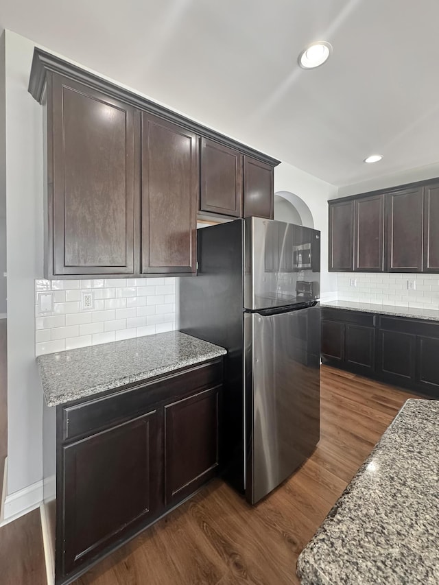 kitchen featuring dark wood-type flooring, dark brown cabinetry, light stone countertops, and stainless steel fridge