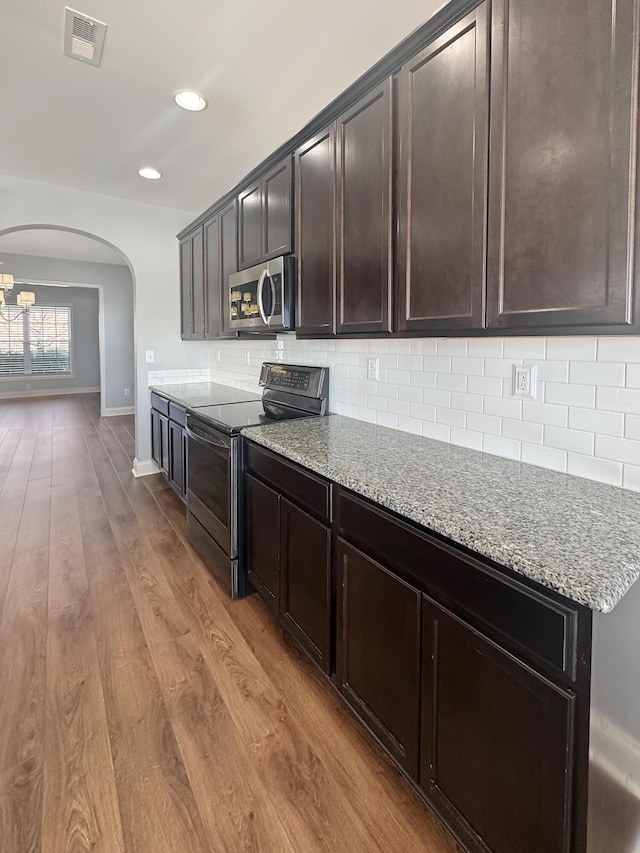 kitchen with light wood-type flooring, dark brown cabinets, light stone counters, appliances with stainless steel finishes, and decorative backsplash