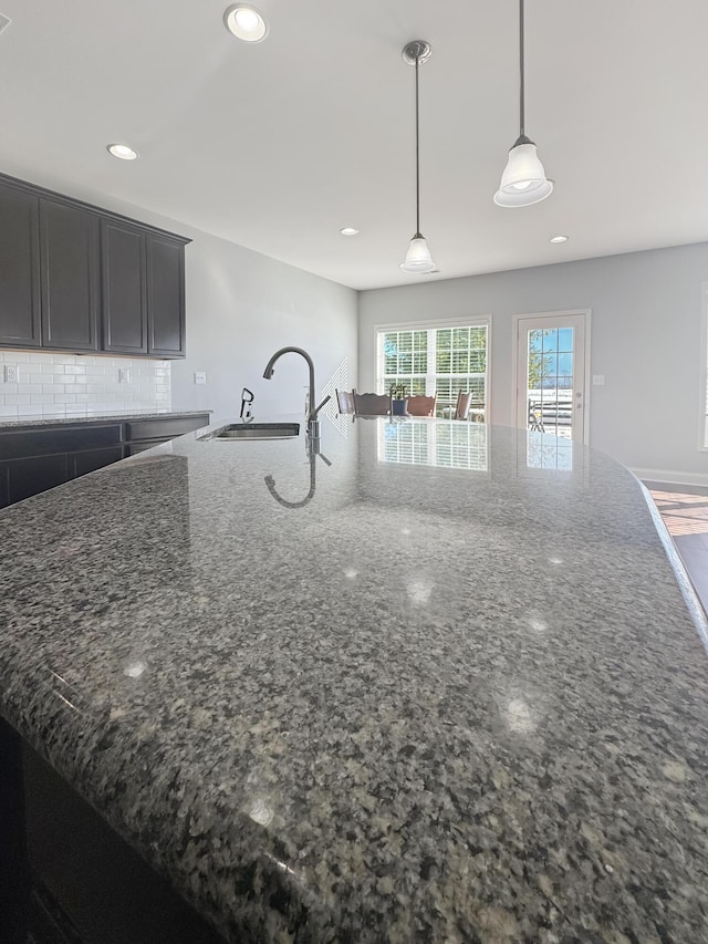 kitchen featuring a center island with sink, decorative backsplash, hanging light fixtures, and dark stone countertops