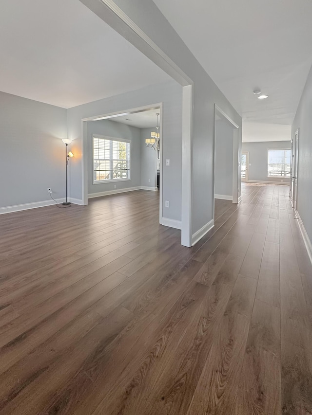 empty room with an inviting chandelier, a wealth of natural light, and dark hardwood / wood-style floors