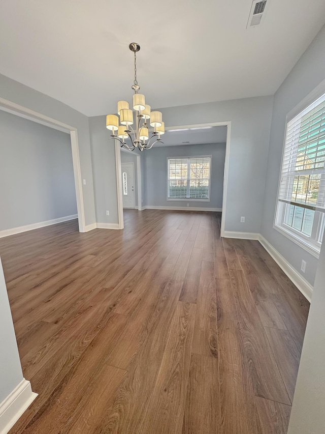 unfurnished dining area featuring a chandelier, a wealth of natural light, and wood-type flooring