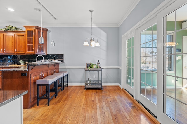 kitchen with pendant lighting, light hardwood / wood-style floors, ornamental molding, decorative backsplash, and dark stone counters