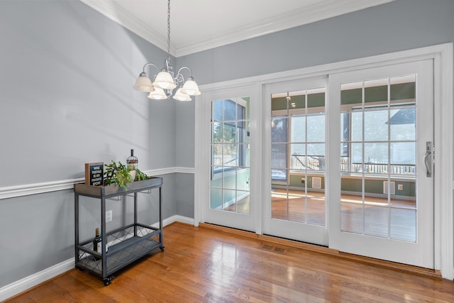 doorway to outside featuring hardwood / wood-style floors, crown molding, and a notable chandelier