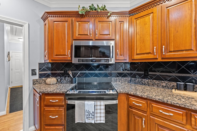 kitchen with crown molding, appliances with stainless steel finishes, dark stone counters, light hardwood / wood-style floors, and backsplash