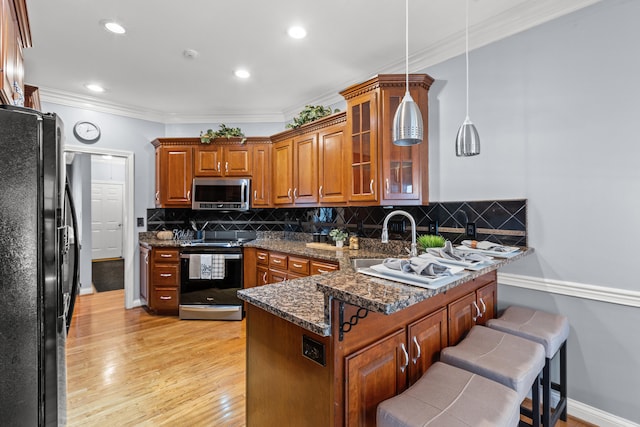 kitchen featuring pendant lighting, sink, dark stone counters, ornamental molding, and stainless steel appliances