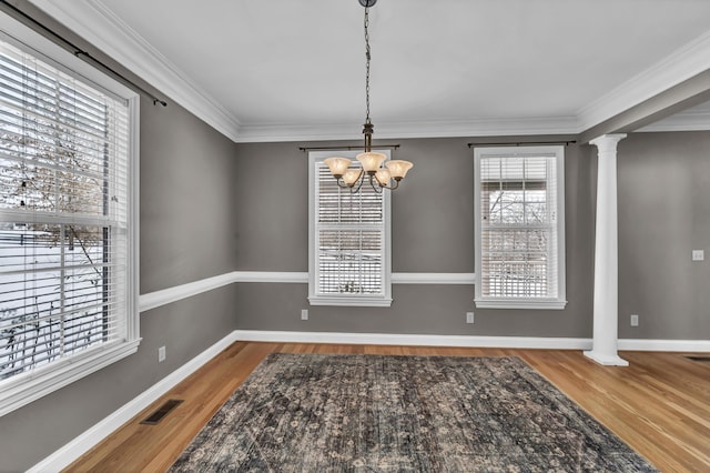 unfurnished dining area featuring wood-type flooring, ornamental molding, ornate columns, and an inviting chandelier