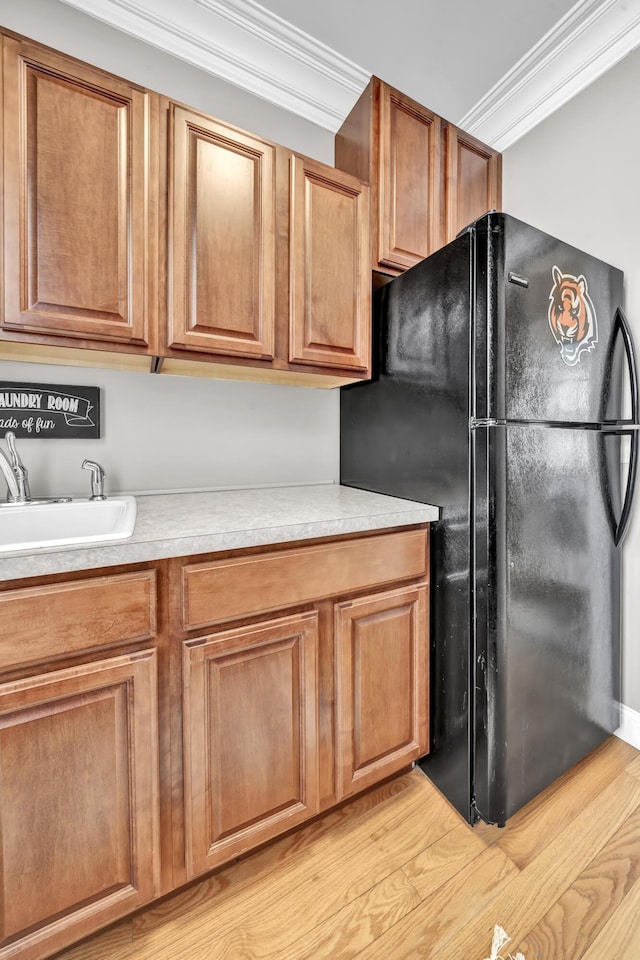 kitchen with black fridge, sink, light hardwood / wood-style flooring, and ornamental molding