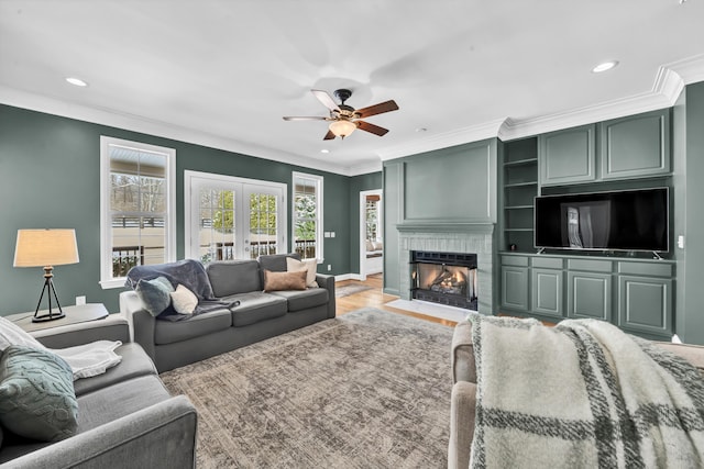 living room featuring hardwood / wood-style flooring, ceiling fan, crown molding, and a fireplace