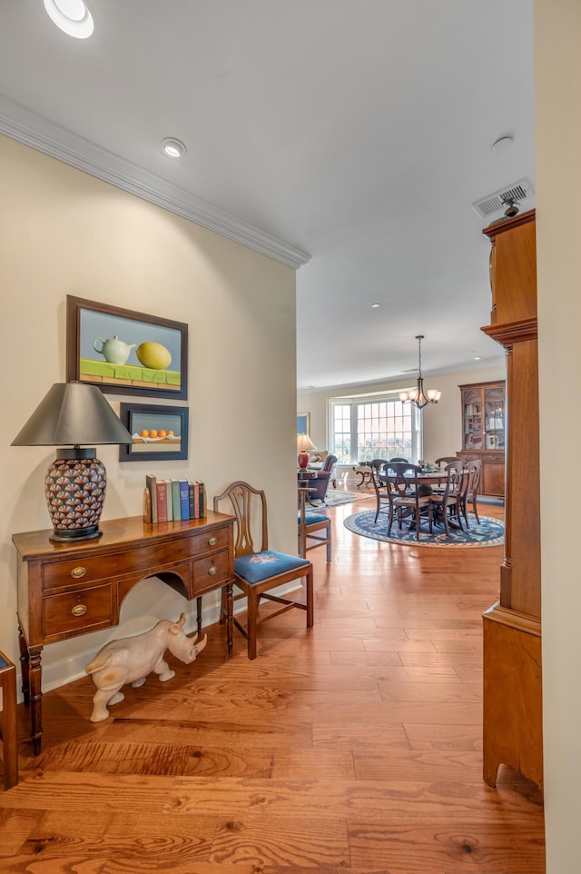 hall with light hardwood / wood-style floors, an inviting chandelier, and crown molding