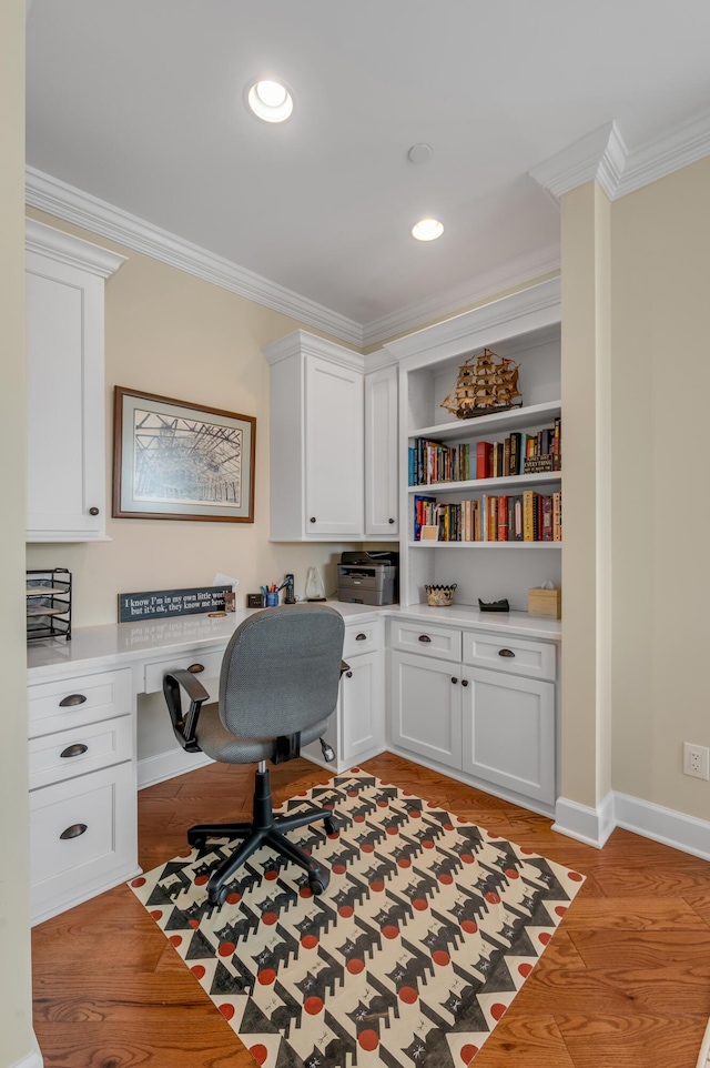 home office with built in desk, light wood-type flooring, and ornamental molding